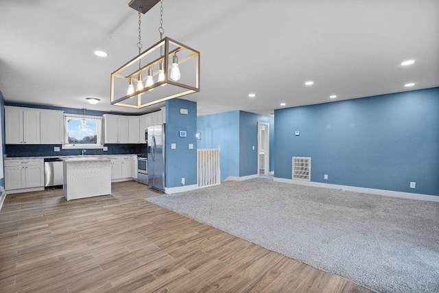 kitchen with pendant lighting, white cabinets, appliances with stainless steel finishes, and light hardwood / wood-style flooring