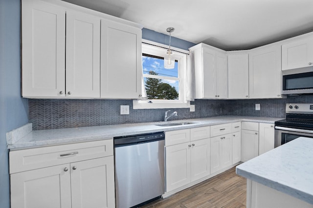 kitchen featuring pendant lighting, hardwood / wood-style floors, sink, white cabinetry, and stainless steel appliances