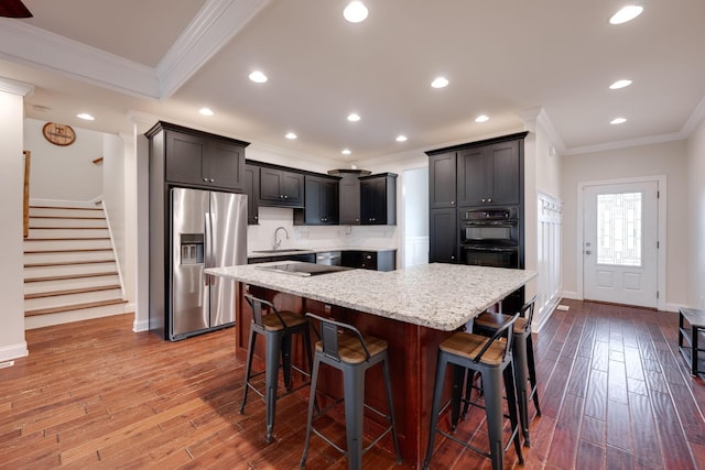 kitchen featuring stainless steel fridge, light stone counters, a breakfast bar, sink, and a center island