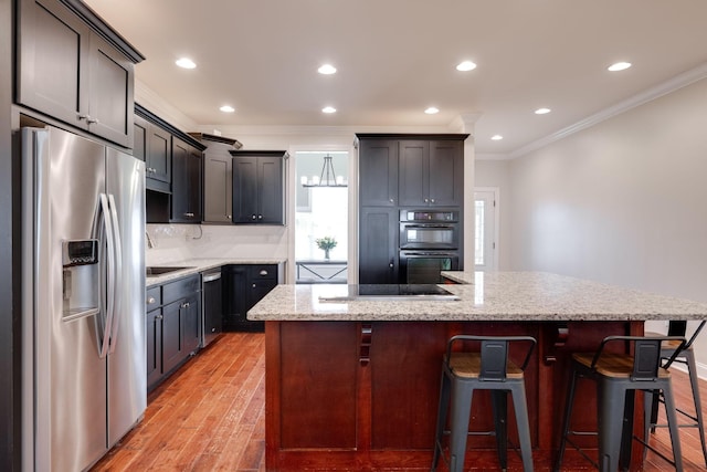 kitchen featuring light stone countertops, an island with sink, crown molding, and black appliances