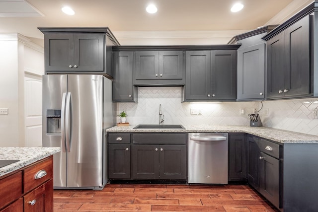 kitchen with stainless steel appliances, a sink, wood finished floors, backsplash, and ornamental molding