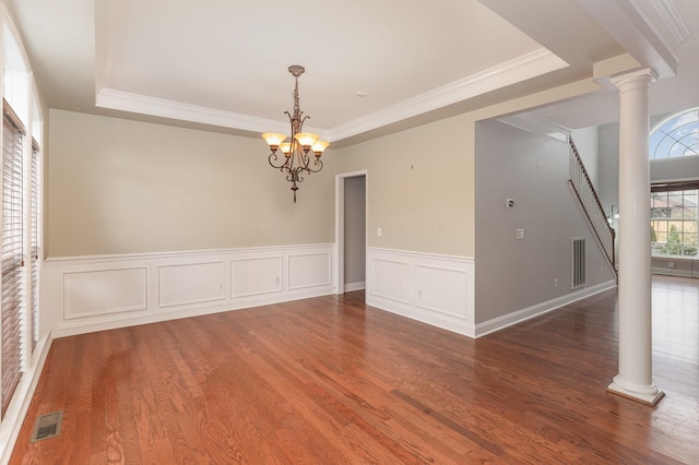 spare room featuring hardwood / wood-style flooring, crown molding, an inviting chandelier, a raised ceiling, and ornate columns