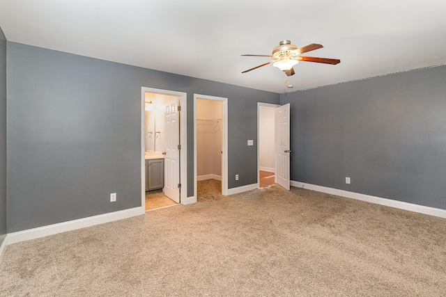 unfurnished bedroom featuring connected bathroom, a walk in closet, light colored carpet, ceiling fan, and a closet