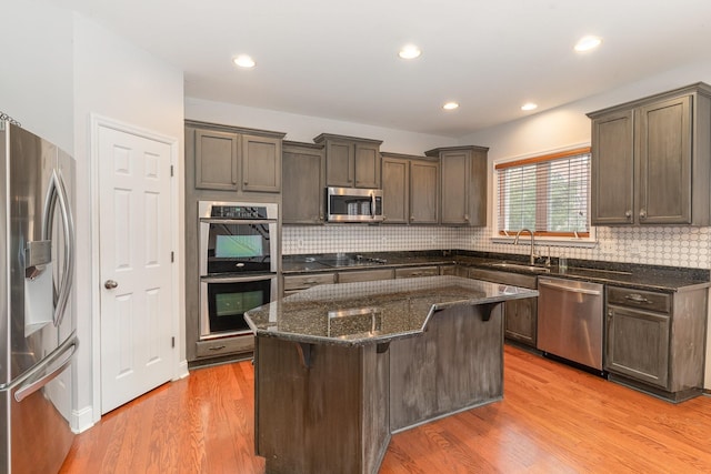 kitchen featuring a center island, light hardwood / wood-style flooring, appliances with stainless steel finishes, a kitchen breakfast bar, and dark stone counters