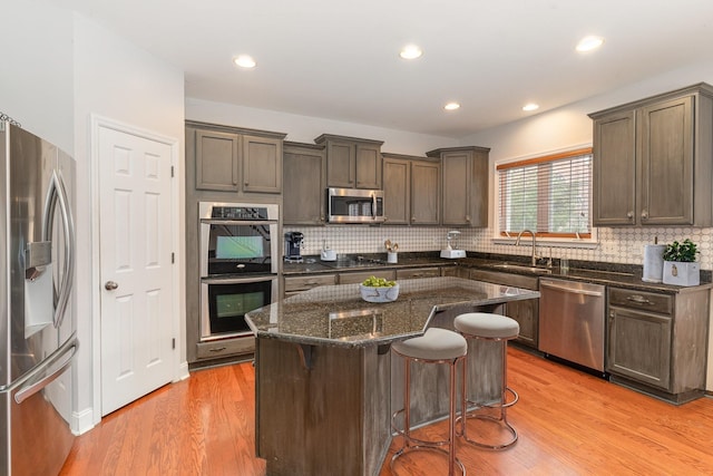 kitchen featuring a breakfast bar area, appliances with stainless steel finishes, dark stone countertops, a center island, and light wood-type flooring