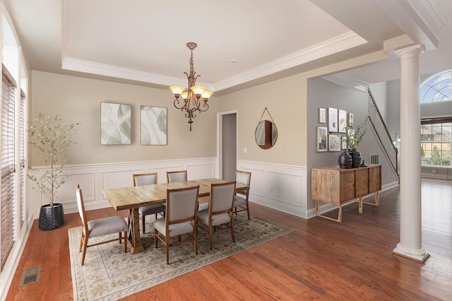 dining space featuring dark hardwood / wood-style floors, decorative columns, a chandelier, ornamental molding, and a tray ceiling