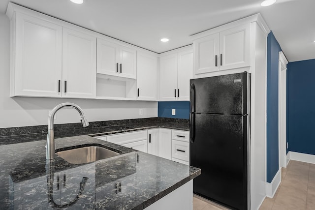 kitchen with sink, light tile patterned floors, black fridge, dark stone counters, and white cabinets