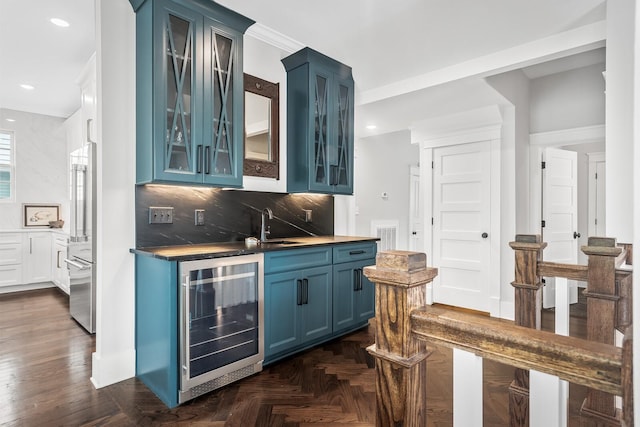 bar featuring blue cabinetry, sink, beverage cooler, backsplash, and ornamental molding