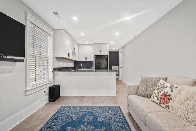 kitchen featuring white cabinets, black refrigerator, light tile patterned flooring, and kitchen peninsula