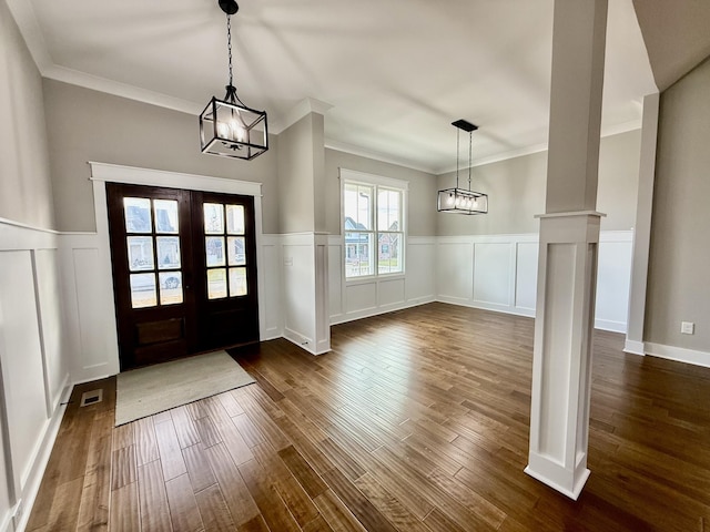 entrance foyer featuring french doors, ornate columns, crown molding, a chandelier, and dark hardwood / wood-style floors