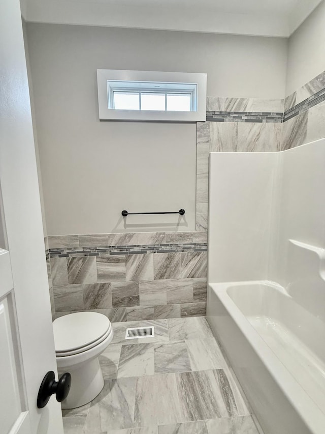 bathroom featuring  shower combination, toilet, and tile walls