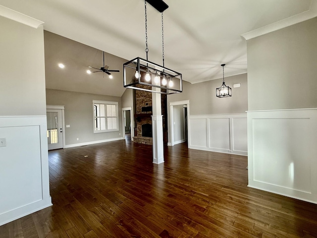 unfurnished living room featuring ceiling fan with notable chandelier, vaulted ceiling, dark wood-type flooring, and a brick fireplace