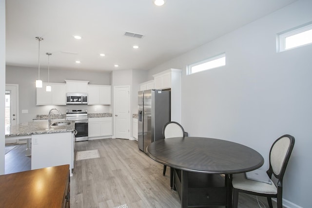 kitchen with hanging light fixtures, light hardwood / wood-style flooring, appliances with stainless steel finishes, light stone counters, and white cabinetry