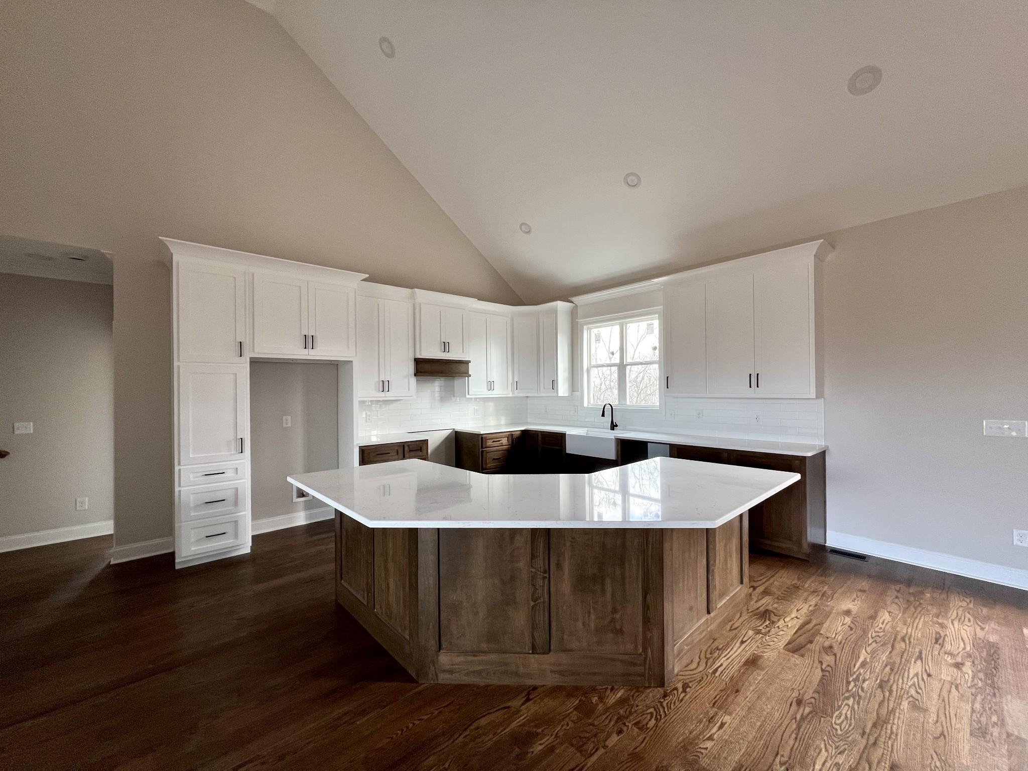 kitchen with white cabinets, high vaulted ceiling, a kitchen island, and dark hardwood / wood-style floors