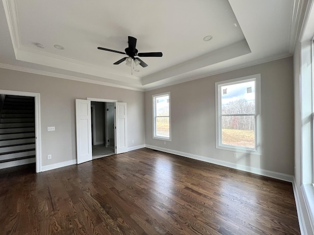 unfurnished bedroom featuring dark hardwood / wood-style floors, ceiling fan, crown molding, and a tray ceiling