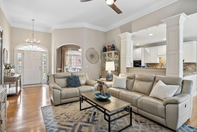 living room with ceiling fan with notable chandelier, light wood-type flooring, and ornamental molding