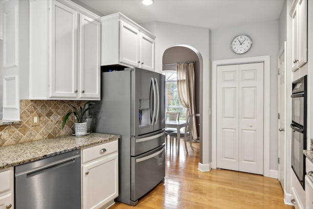 kitchen featuring tasteful backsplash, light stone counters, appliances with stainless steel finishes, white cabinets, and light wood-type flooring