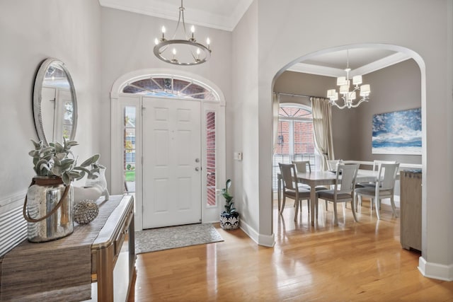 foyer entrance with crown molding, light hardwood / wood-style floors, and an inviting chandelier