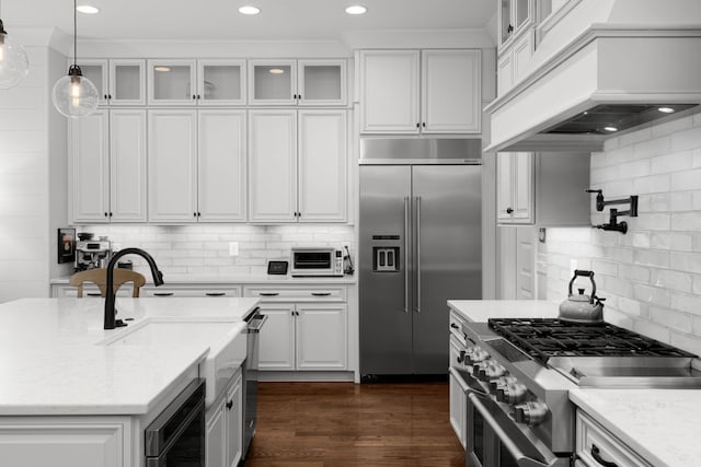 kitchen with white cabinets, custom exhaust hood, high end appliances, hanging light fixtures, and light stone counters