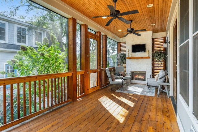 unfurnished sunroom with ceiling fan, a brick fireplace, and wood ceiling