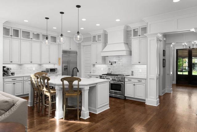 kitchen featuring premium range hood, white cabinetry, high end appliances, tasteful backsplash, and an island with sink