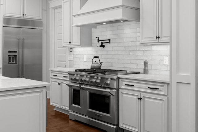 kitchen featuring white cabinetry, premium appliances, dark hardwood / wood-style floors, custom range hood, and backsplash