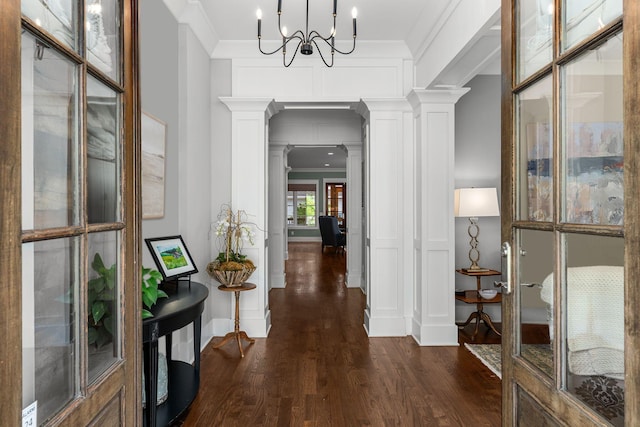 corridor with crown molding, dark hardwood / wood-style flooring, an inviting chandelier, and ornate columns