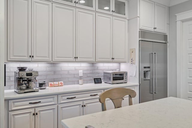 kitchen with backsplash, built in refrigerator, light stone countertops, and white cabinets