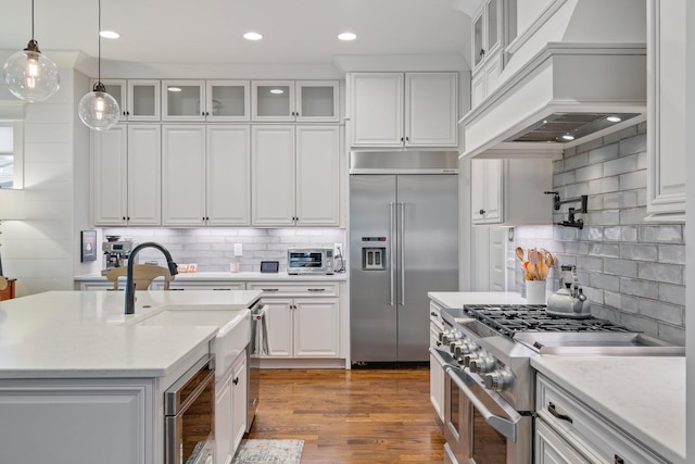 kitchen with white cabinetry, custom range hood, built in appliances, and decorative light fixtures