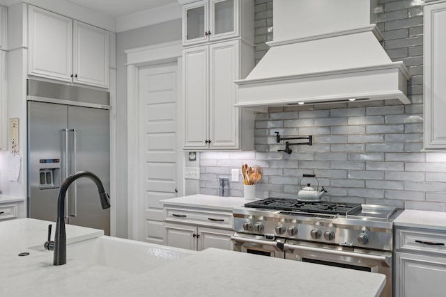 kitchen with sink, custom exhaust hood, high end appliances, white cabinets, and backsplash