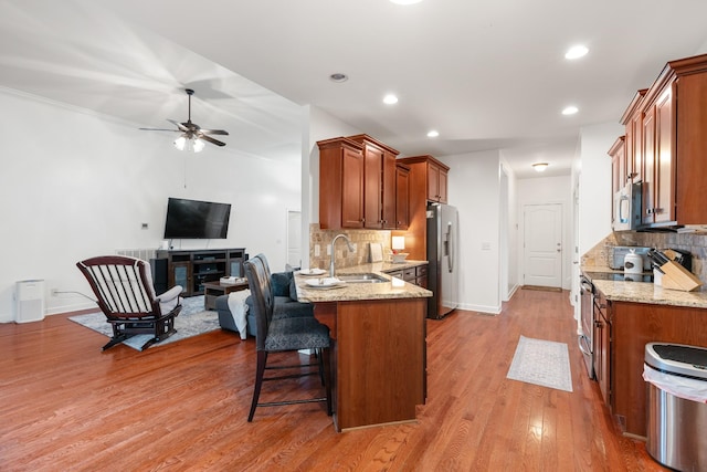 kitchen featuring ceiling fan, sink, backsplash, appliances with stainless steel finishes, and light wood-type flooring