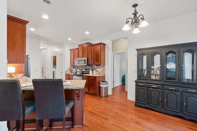 kitchen with light stone counters, backsplash, a chandelier, appliances with stainless steel finishes, and light wood-type flooring