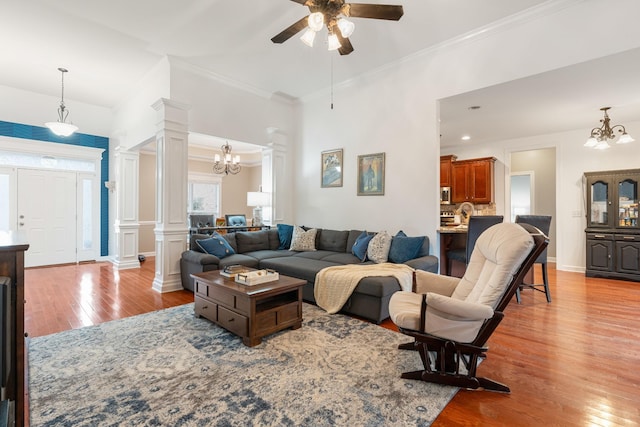 living room with ceiling fan with notable chandelier, light hardwood / wood-style floors, ornate columns, and ornamental molding