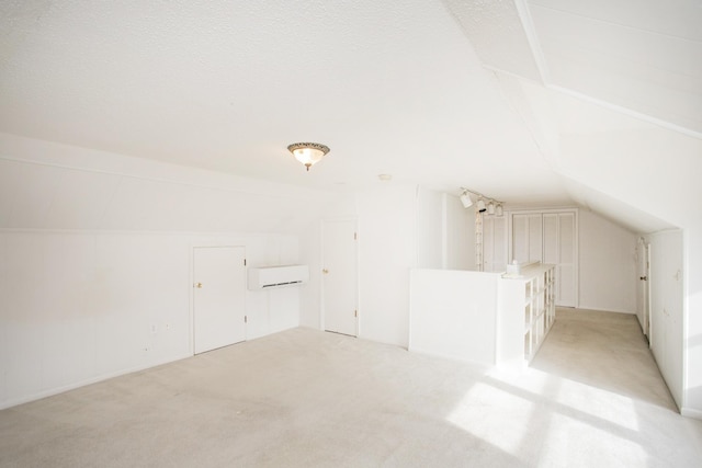 additional living space featuring a textured ceiling, light carpet, a wall unit AC, and vaulted ceiling