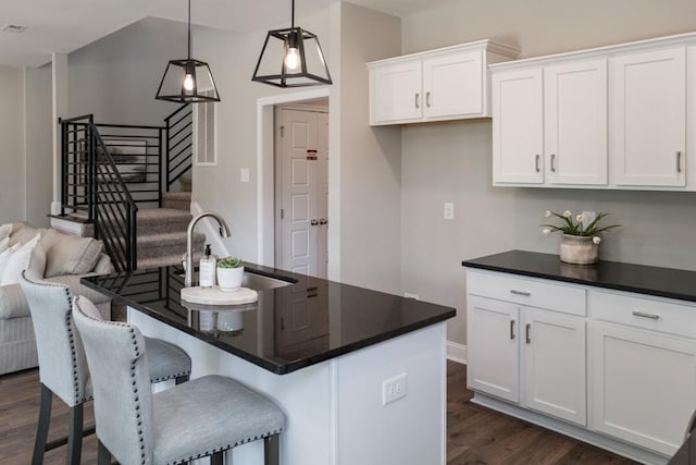 kitchen featuring white cabinetry, sink, dark wood-type flooring, an island with sink, and decorative light fixtures