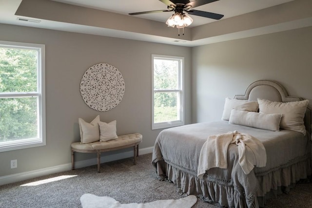 carpeted bedroom with a tray ceiling, multiple windows, and ceiling fan