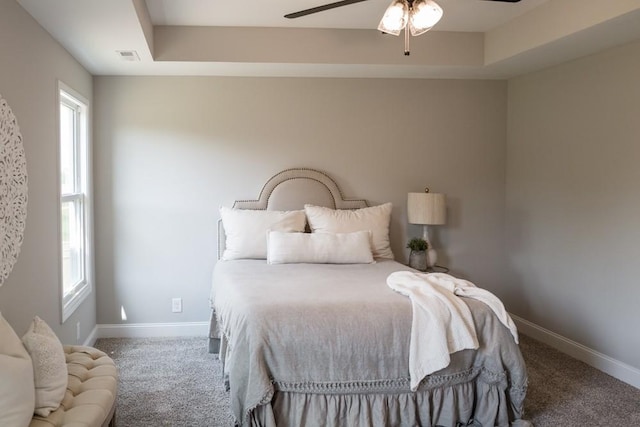 carpeted bedroom with a raised ceiling and ceiling fan