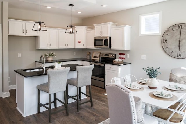 kitchen with appliances with stainless steel finishes, a kitchen island with sink, dark wood-type flooring, white cabinetry, and hanging light fixtures