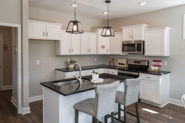 kitchen featuring a center island with sink, hanging light fixtures, sink, appliances with stainless steel finishes, and white cabinetry