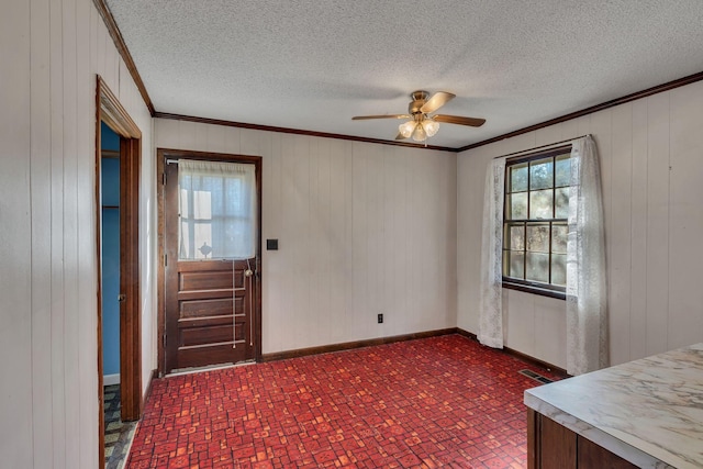 entrance foyer with ceiling fan, wooden walls, and crown molding