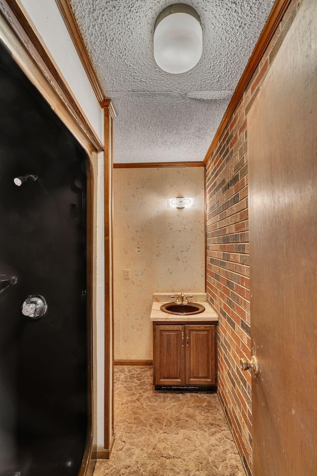 bathroom with vanity, a textured ceiling, ornamental molding, and brick wall