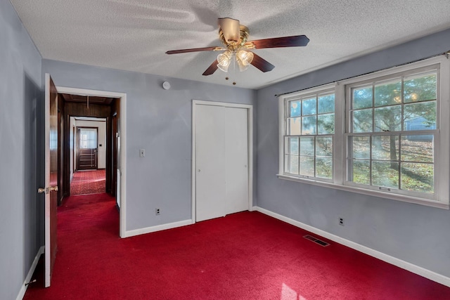 unfurnished bedroom featuring dark colored carpet, ceiling fan, a textured ceiling, and a closet