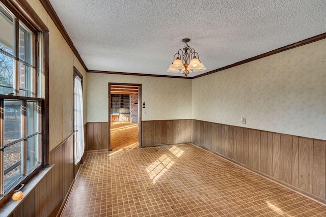 spare room with a textured ceiling, an inviting chandelier, crown molding, and wood walls