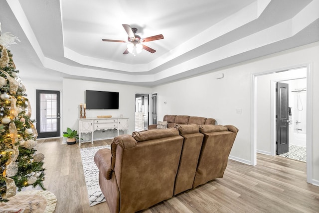 living room featuring a tray ceiling, ceiling fan, and light hardwood / wood-style floors