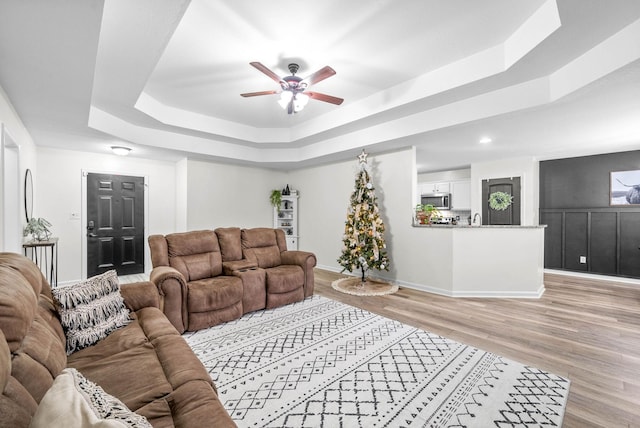 living room featuring a tray ceiling, ceiling fan, and light wood-type flooring