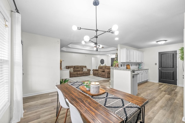 dining space with a raised ceiling, an inviting chandelier, and light wood-type flooring