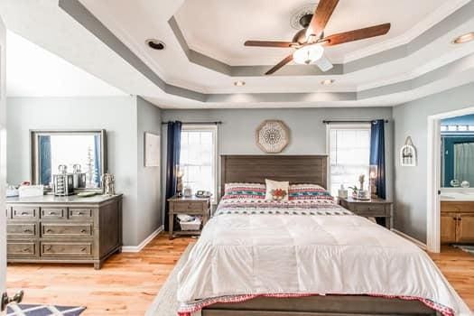 bedroom featuring ceiling fan, connected bathroom, a tray ceiling, and light wood-type flooring