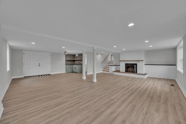 unfurnished living room featuring recessed lighting, light wood-style floors, a fireplace, baseboards, and stairs