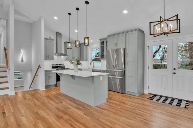 kitchen with stainless steel appliances, wall chimney exhaust hood, gray cabinets, and light countertops