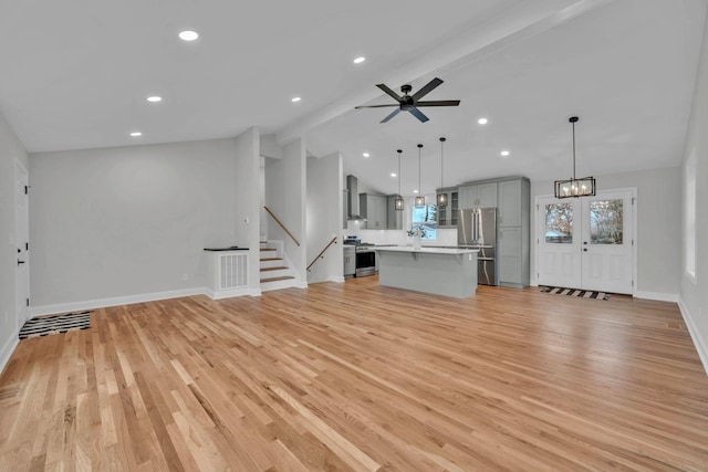 unfurnished living room with visible vents, light wood-style flooring, ceiling fan with notable chandelier, lofted ceiling with beams, and stairs